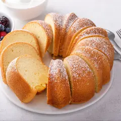 Wilgotna babka piaskowa, oprószona cukrem pudrem, prezentuje się apetycznie obok miseczki z jagodami i malinami.
