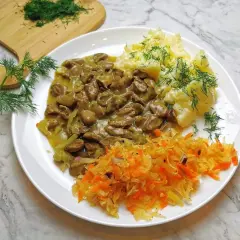 Pyszny gulasz z serc drobiowych z puree ziemniaczanym i surówką z kiszonej kapusty, ozdobiony świeżym koperkiem.