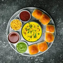 Talerz z Vada Pav: żółty curry, zielony chutney, czerwona przyprawa, żółta fasolka, brązowy sos i bułeczki. Chutney co to? To dodatek do dania.