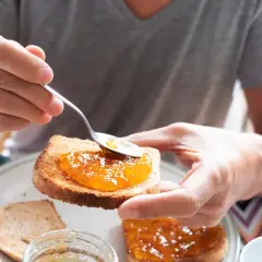 Osoba smaruje łyżeczką tost aromatycznym dżemem z nektarynek. Pyszny początek dnia!