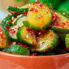 Pikantne ogórki z chili i czosnkiem na zimę, w glinianej miseczce, posypane sezamem.