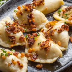 Pierogi z serem, przygotowane według przepisu babci, polane skwarkami i szczypiorkiem, na czarnej patelni.