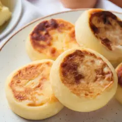 Szybkie placuszki serowe z budyniem, rumiane i puszyste, idealne na śniadanie. Obok talerzyk z masłem.