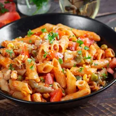 Penne z kurczakiem, pomidorami, groszkiem i pieczarkami w sosie pomidorowym. Pyszny obiad z pieczarkami, posypany parmezanem i natką pietruszki.