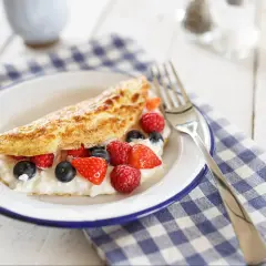 Lekki omlet z białek z serkiem i świeżymi malinami, borówkami i truskawkami na talerzu.