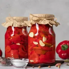 Słoiki z papryką marynowaną według przepisu babci. W tle świeża papryka, czosnek i przyprawy.