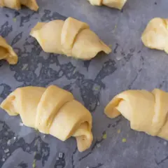 Surowe rogaliki krucho drożdżowe, gotowe do pieczenia, leżą na papierze do pieczenia.