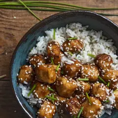 Apetyczne dania z tofu w sosie, posypane sezamem i szczypiorkiem, podane z ryżem.