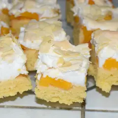 Puszyste ciasto z brzoskwiniami, przełożone pianką i posypane płatkami migdałów.