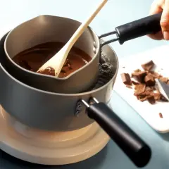 Krok po kroku, jak rozpuścić czekoladę w kąpieli wodnej. Drewniana łyżka miesza płynną czekoladę w garnku.