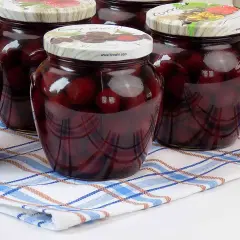 Słoiki z kompotem z czereśni na zimę, pełne ciemnych owoców w słodkim syropie, gotowe do otwarcia w chłodne dni.