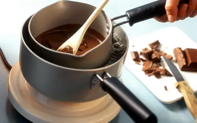 Krok po kroku, jak rozpuścić czekoladę w kąpieli wodnej. Drewniana łyżka miesza płynną czekoladę w garnku.