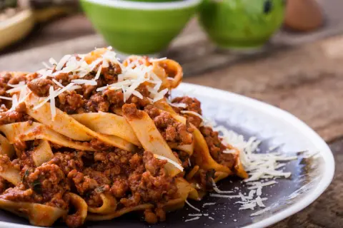 Pappardelle z bogatym sosem bolognese, idealne pytanie: jakie mięso do spaghetti? Posypane parmezanem.