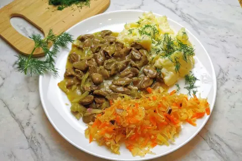 Pyszny gulasz z serc drobiowych z puree ziemniaczanym i surówką z kiszonej kapusty, ozdobiony świeżym koperkiem.