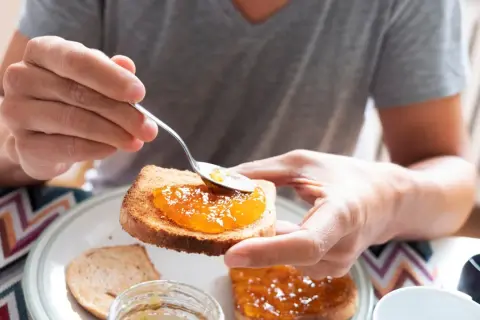 Osoba smaruje łyżeczką tost aromatycznym dżemem z nektarynek. Pyszny początek dnia!