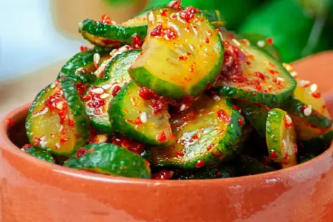 Pikantne ogórki z chili i czosnkiem na zimę, w glinianej miseczce, posypane sezamem.