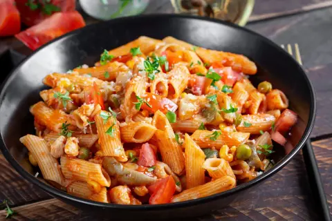 Penne z kurczakiem, pomidorami, groszkiem i pieczarkami w sosie pomidorowym. Pyszny obiad z pieczarkami, posypany parmezanem i natką pietruszki.