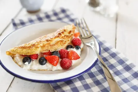 Lekki omlet z białek z serkiem i świeżymi malinami, borówkami i truskawkami na talerzu.