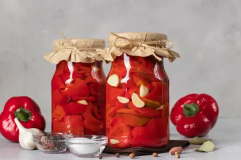 Słoiki z papryką marynowaną według przepisu babci. W tle świeża papryka, czosnek i przyprawy.