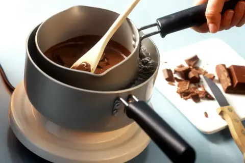 Krok po kroku, jak rozpuścić czekoladę w kąpieli wodnej. Drewniana łyżka miesza płynną czekoladę w garnku.