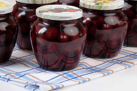 Słoiki z kompotem z czereśni na zimę, pełne ciemnych owoców w słodkim syropie, gotowe do otwarcia w chłodne dni.