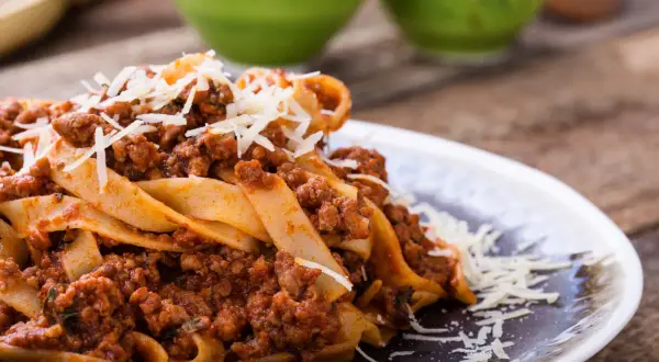 Pappardelle z bogatym sosem bolognese, idealne pytanie: jakie mięso do spaghetti? Posypane parmezanem.