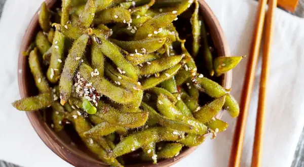 Miseczka pełna zielonych strączków edamame, posypanych sezamem. Idealna przekąska, która wyjaśnia, edamame co to jest.