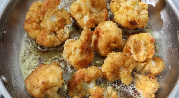 Chrupiące różyczki kalafiora w panierce smażą się na złoto w metalowej patelni, tworząc apetyczny przysmak.