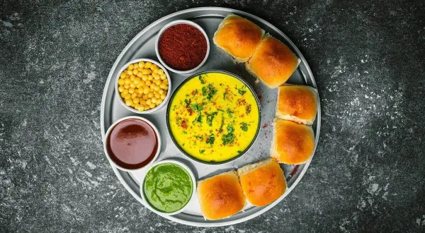 Talerz z Vada Pav: żółty curry, zielony chutney, czerwona przyprawa, żółta fasolka, brązowy sos i bułeczki. Chutney co to? To dodatek do dania.