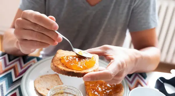 Osoba smaruje łyżeczką tost aromatycznym dżemem z nektarynek. Pyszny początek dnia!