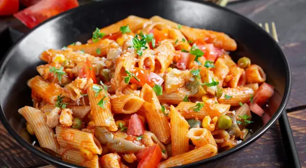 Penne z kurczakiem, pomidorami, groszkiem i pieczarkami w sosie pomidorowym. Pyszny obiad z pieczarkami, posypany parmezanem i natką pietruszki.