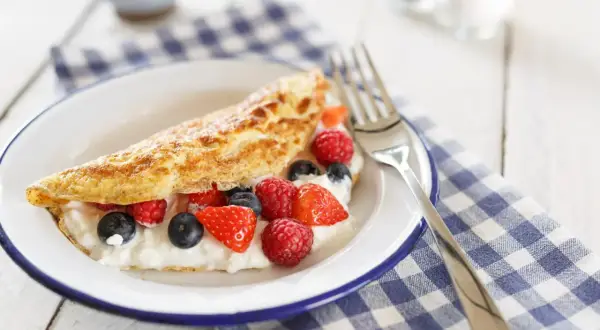 Lekki omlet z białek z serkiem i świeżymi malinami, borówkami i truskawkami na talerzu.