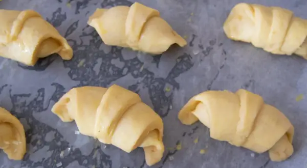 Surowe rogaliki krucho drożdżowe, gotowe do pieczenia, leżą na papierze do pieczenia.