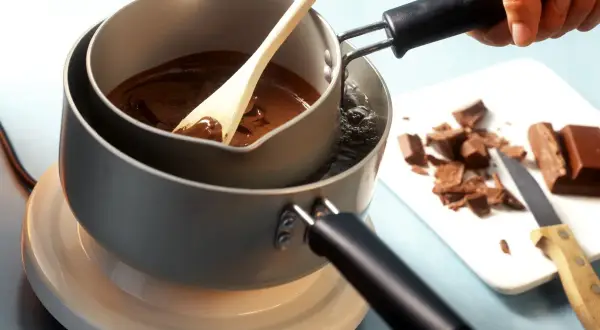 Krok po kroku, jak rozpuścić czekoladę w kąpieli wodnej. Drewniana łyżka miesza płynną czekoladę w garnku.