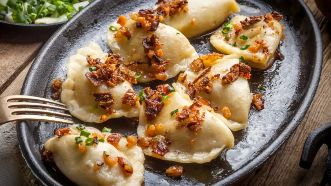 Pierogi z serem, przygotowane według przepisu babci, polane skwarkami i szczypiorkiem, na czarnej patelni.
