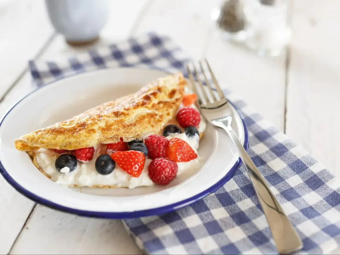 Lekki omlet z białek z serkiem i świeżymi malinami, borówkami i truskawkami na talerzu.