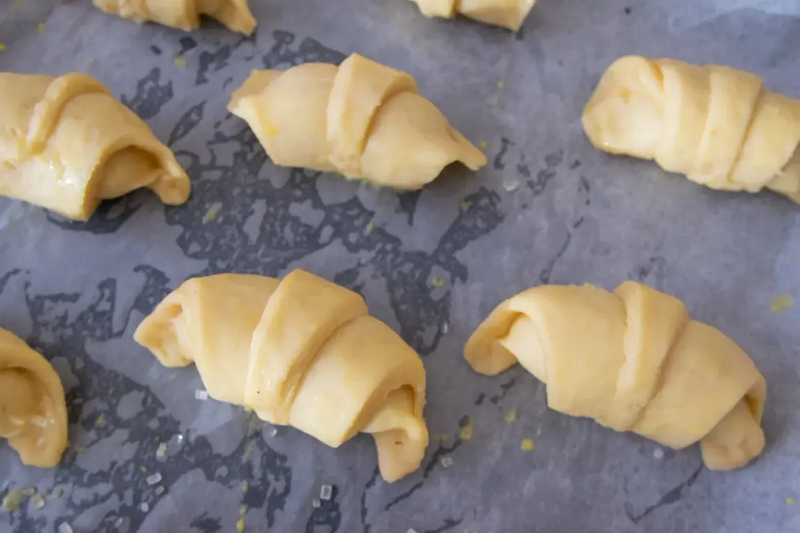 Surowe rogaliki krucho drożdżowe, gotowe do pieczenia, leżą na papierze do pieczenia.