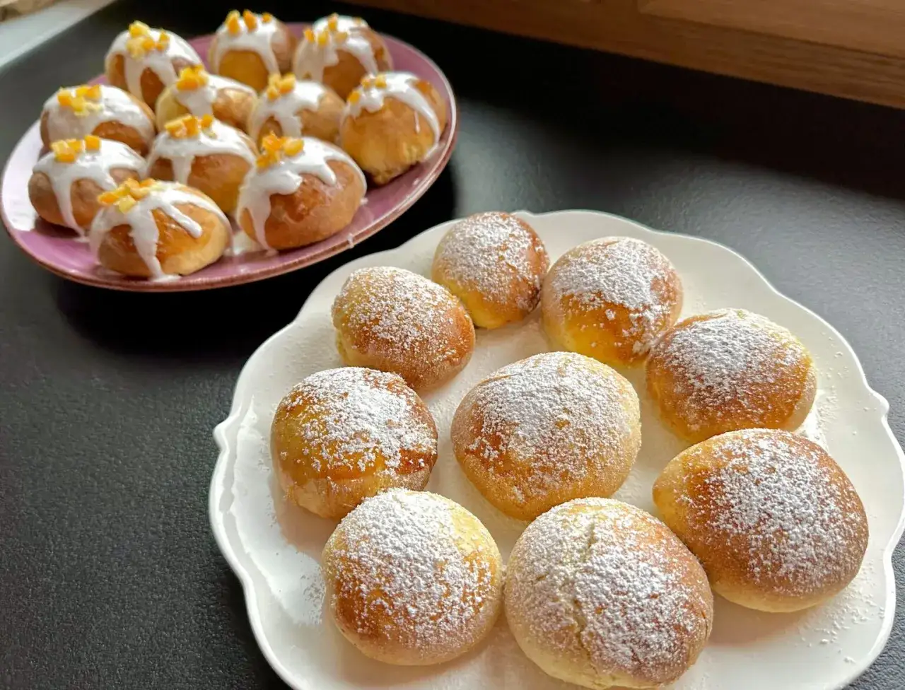 Pyszne pączki z piekarnika, jedne opr&oacute;szone cukrem pudrem, drugie polane lukrem i posypane sk&oacute;rką pomarańczową.
