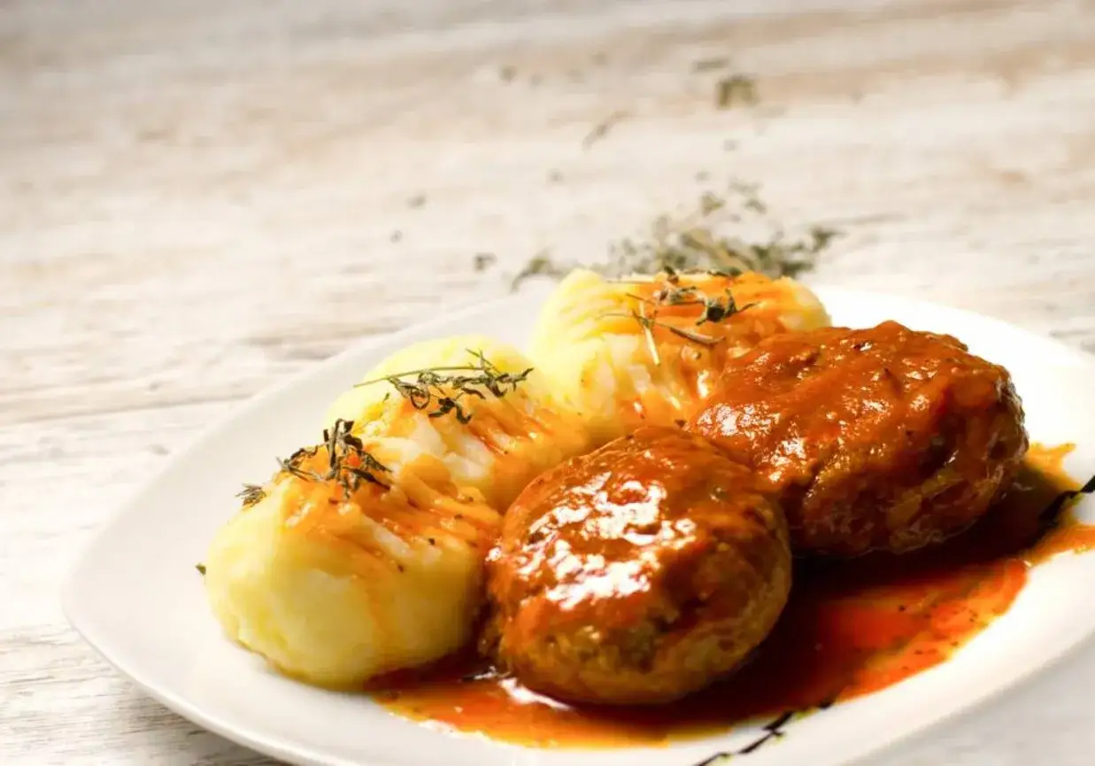Pyszne mielone w sosie pomidorowym, podane z pur&eacute;e ziemniaczanym i ziołami.