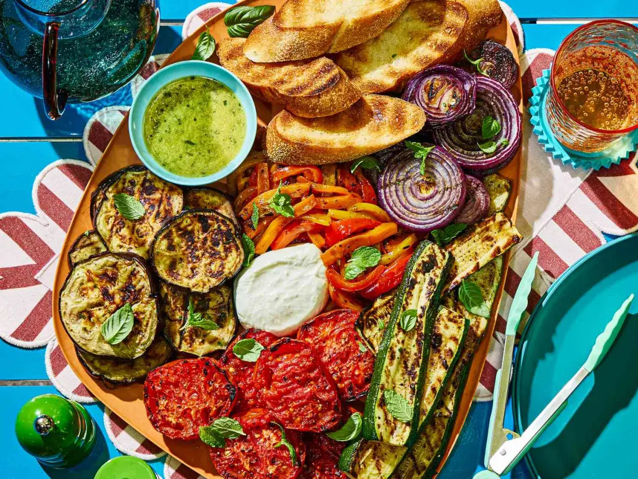 Kolorowa deska pełna grillowanych warzyw: cukinii, bakłażana, papryki, cebuli i pomidorów. Idealne przystawki do grilla z sosem i pieczywem.