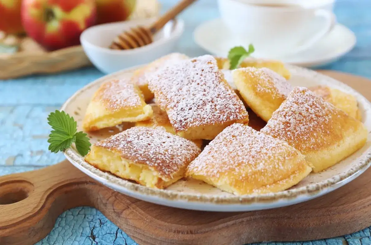 Puszysty omlet z jabłkiem, posypany cukrem pudrem, na talerzu z listkiem mięty. Idealny na deser.