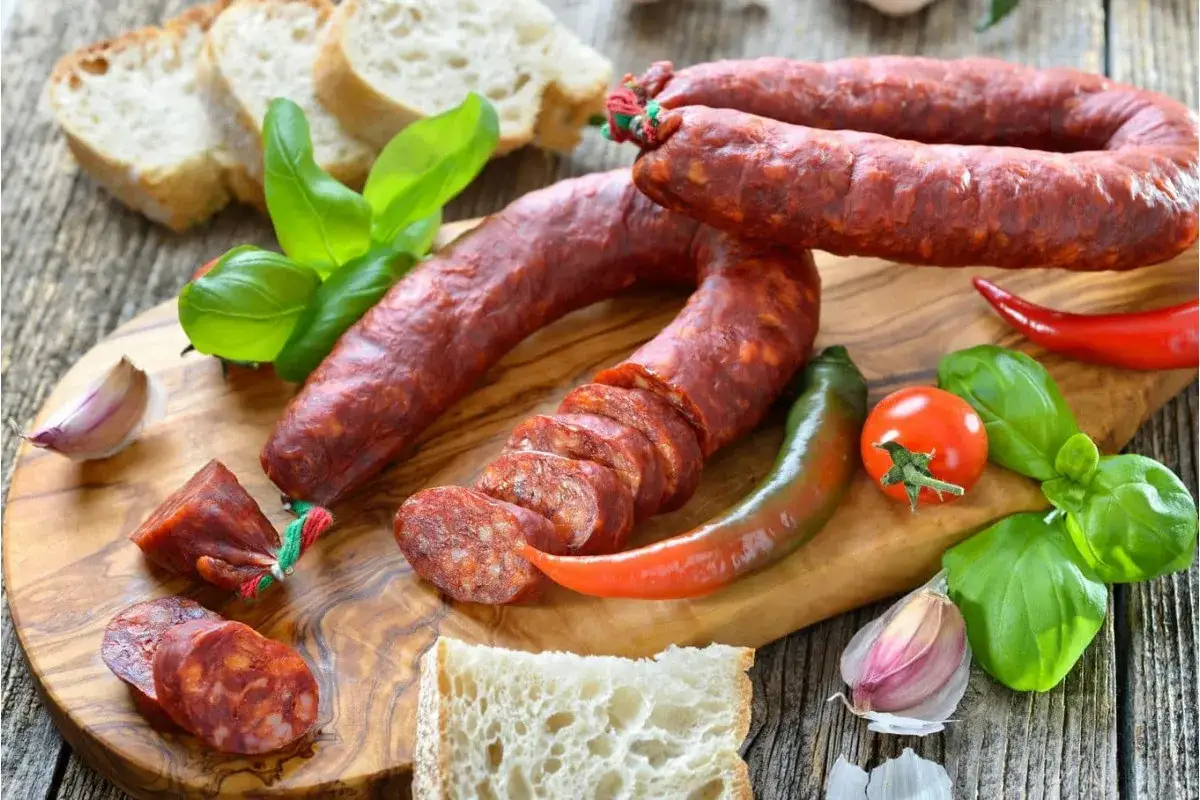 Chorizo co to? Pikantna kiełbasa, chleb, papryczki, pomidor i bazylia na desce. Idealne składniki na przekąskę.