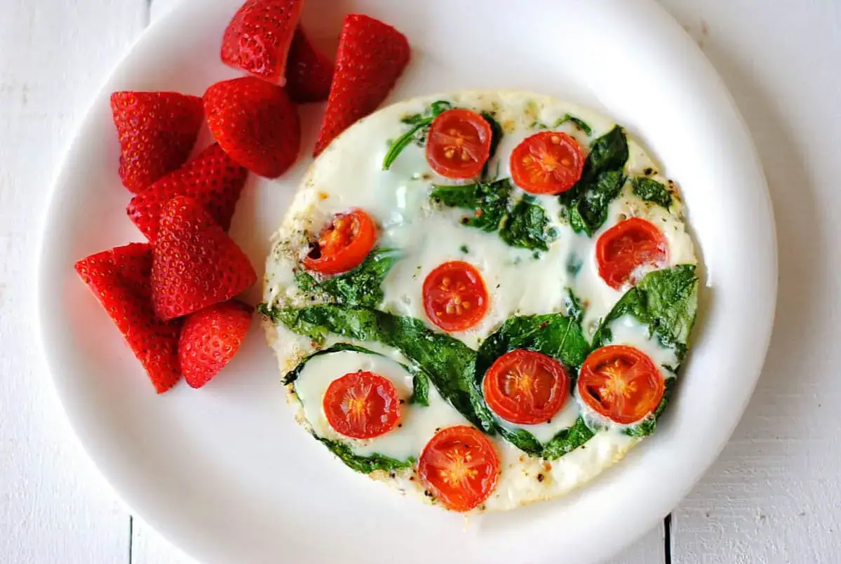 Zdrowy omlet z białek z pomidorkami i szpinakiem, podany z poł&oacute;wkami truskawek. Idealny na lekki posiłek.