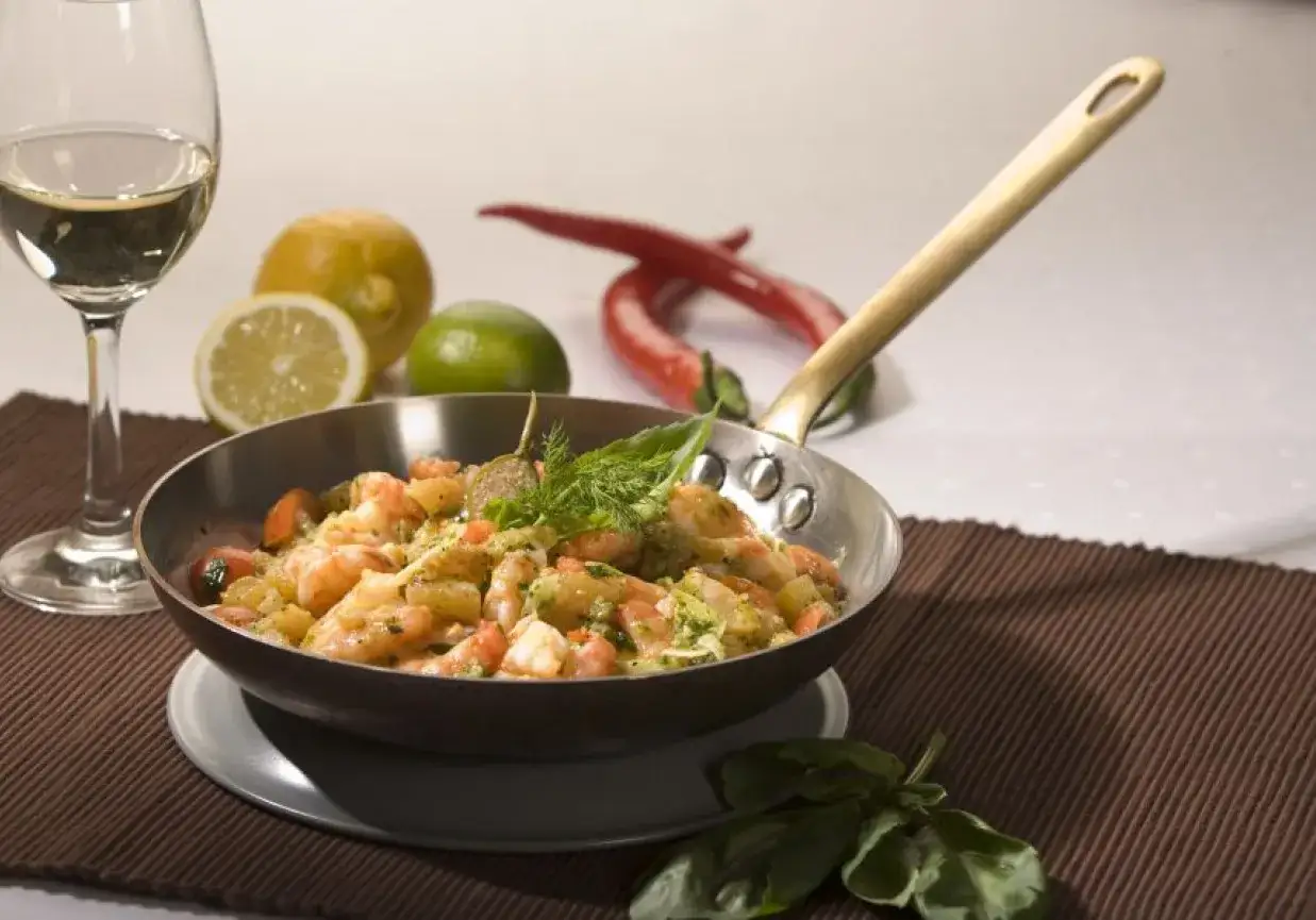 Pyszne krewetki z grilla w sosie, podane w patelni z dodatkiem cytryny, limonki i papryczek chili.
