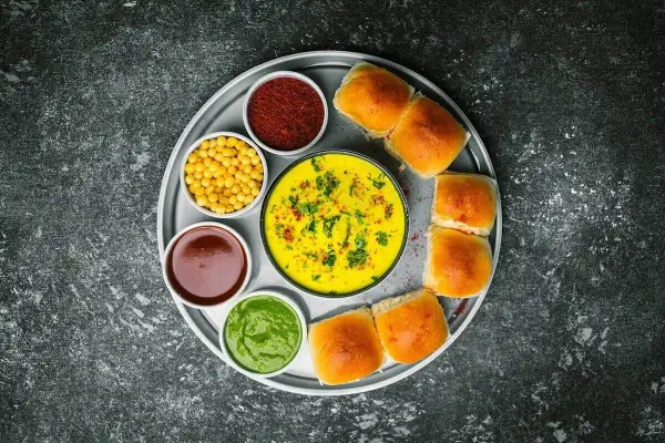 Talerz z Vada Pav: żółty curry, zielony chutney, czerwona przyprawa, żółta fasolka, brązowy sos i bułeczki. Chutney co to? To dodatek do dania.
