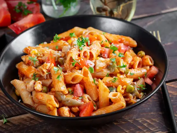 Penne z kurczakiem, pomidorami, groszkiem i pieczarkami w sosie pomidorowym. Pyszny obiad z pieczarkami, posypany parmezanem i natką pietruszki.