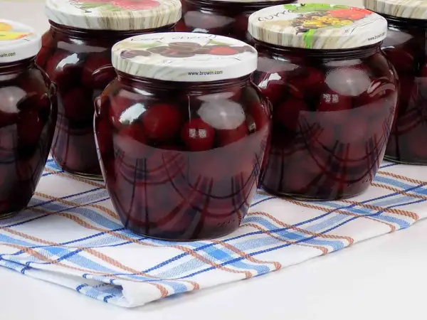 Słoiki z kompotem z czereśni na zimę, pełne ciemnych owoców w słodkim syropie, gotowe do otwarcia w chłodne dni.